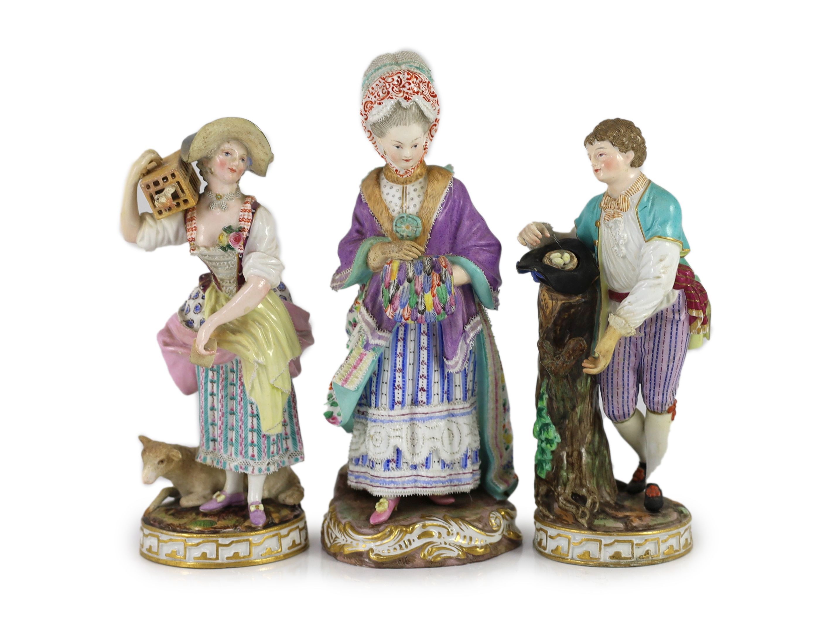 A pair of Meissen figures of a youth with a bird’s nest and a maiden holding a bird in a cage and a Meissen figure of a lady with a muff, 19th century, 18.5 - 20.5cm high, some restoration and losses